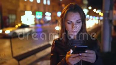 迷人的女人在夜城的<strong>街道</strong>上<strong>行走</strong>时使用智能手机
